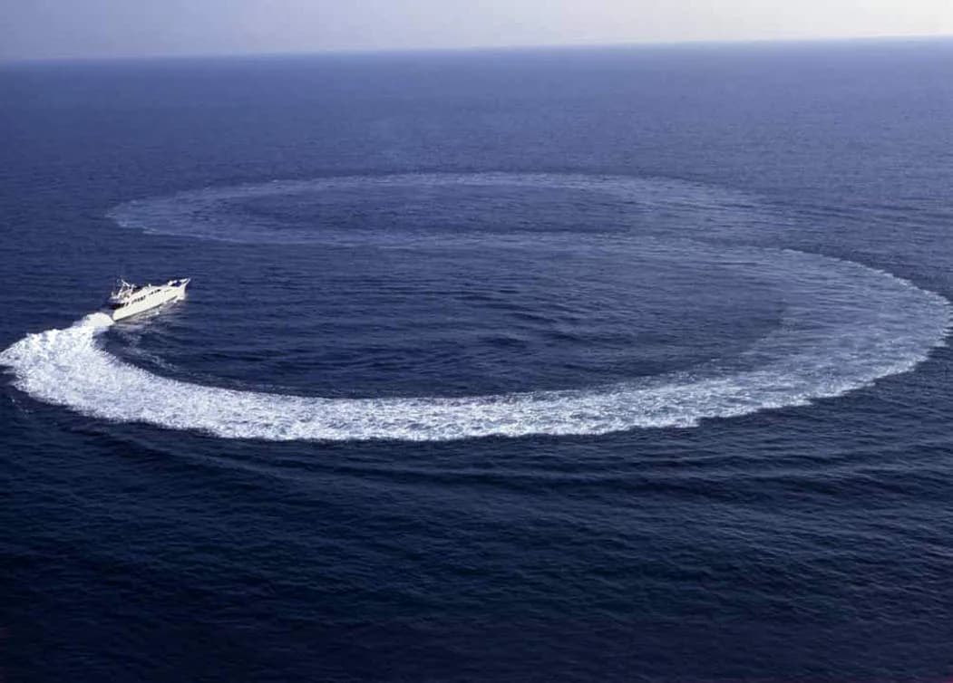 A white motor yacht turning a full circle of wake on open blue water