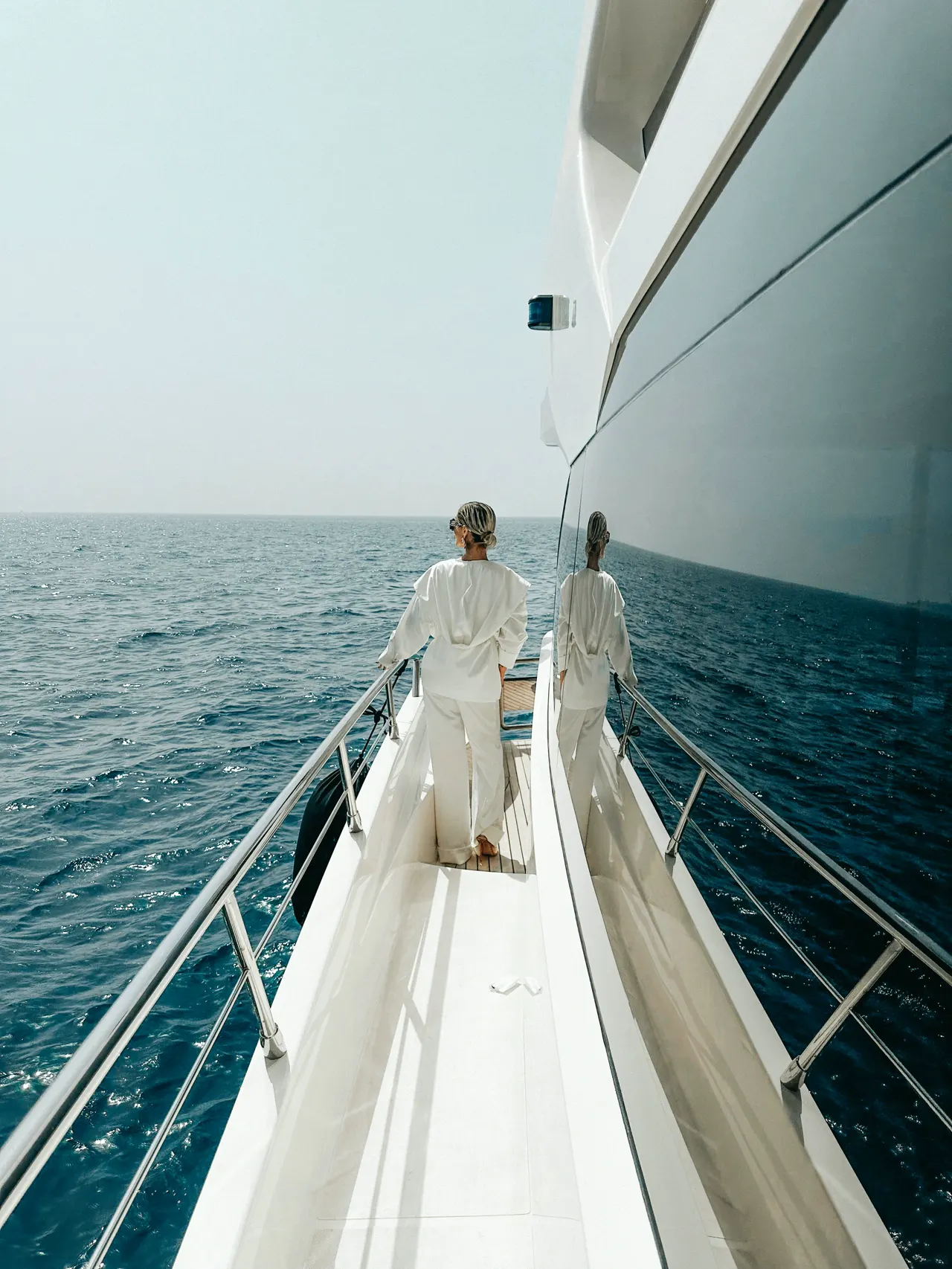 A guest in white linen walking the side deck of a motor yacht at sea