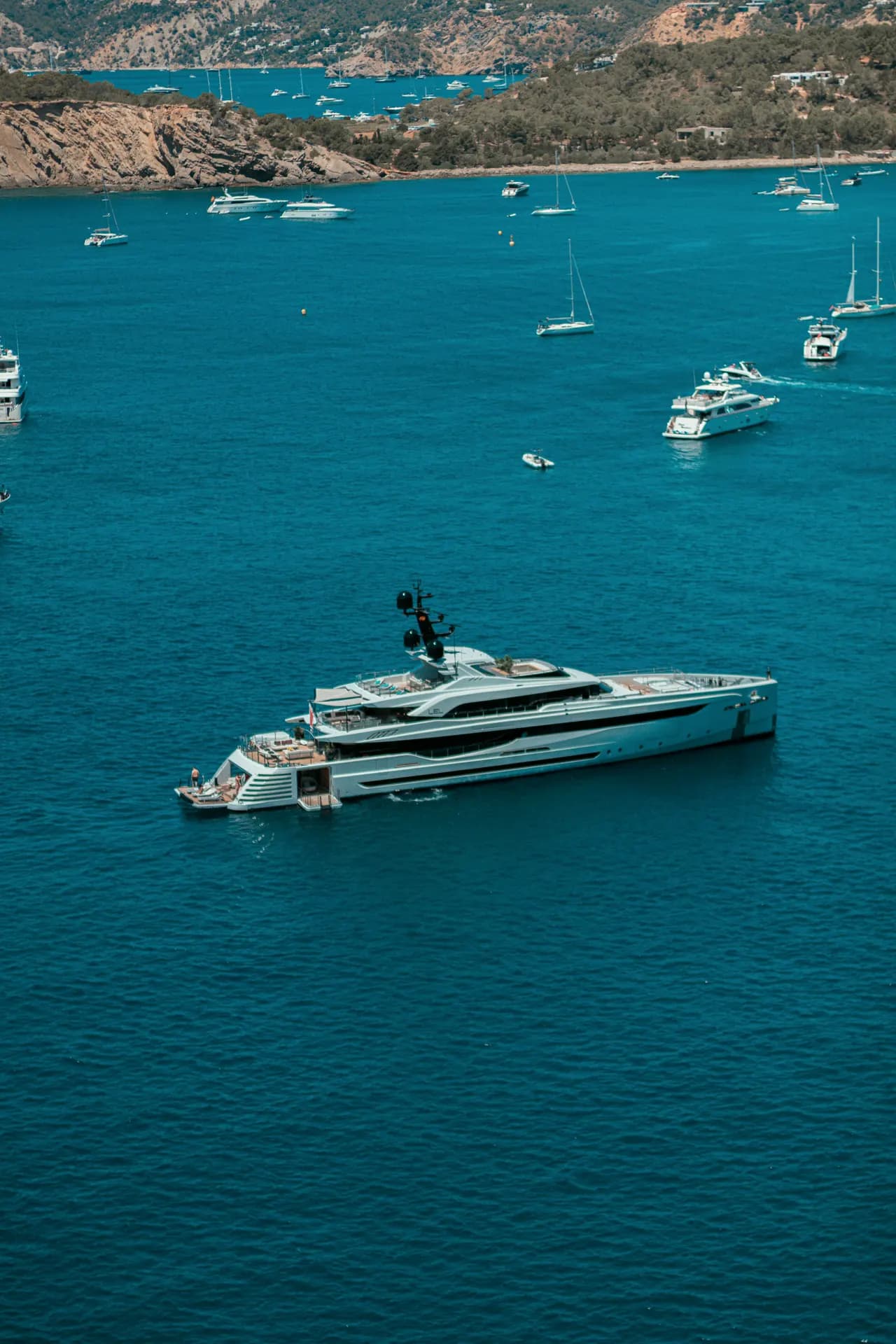 A modern motor yacht at anchor in a deep blue bay, seen from above