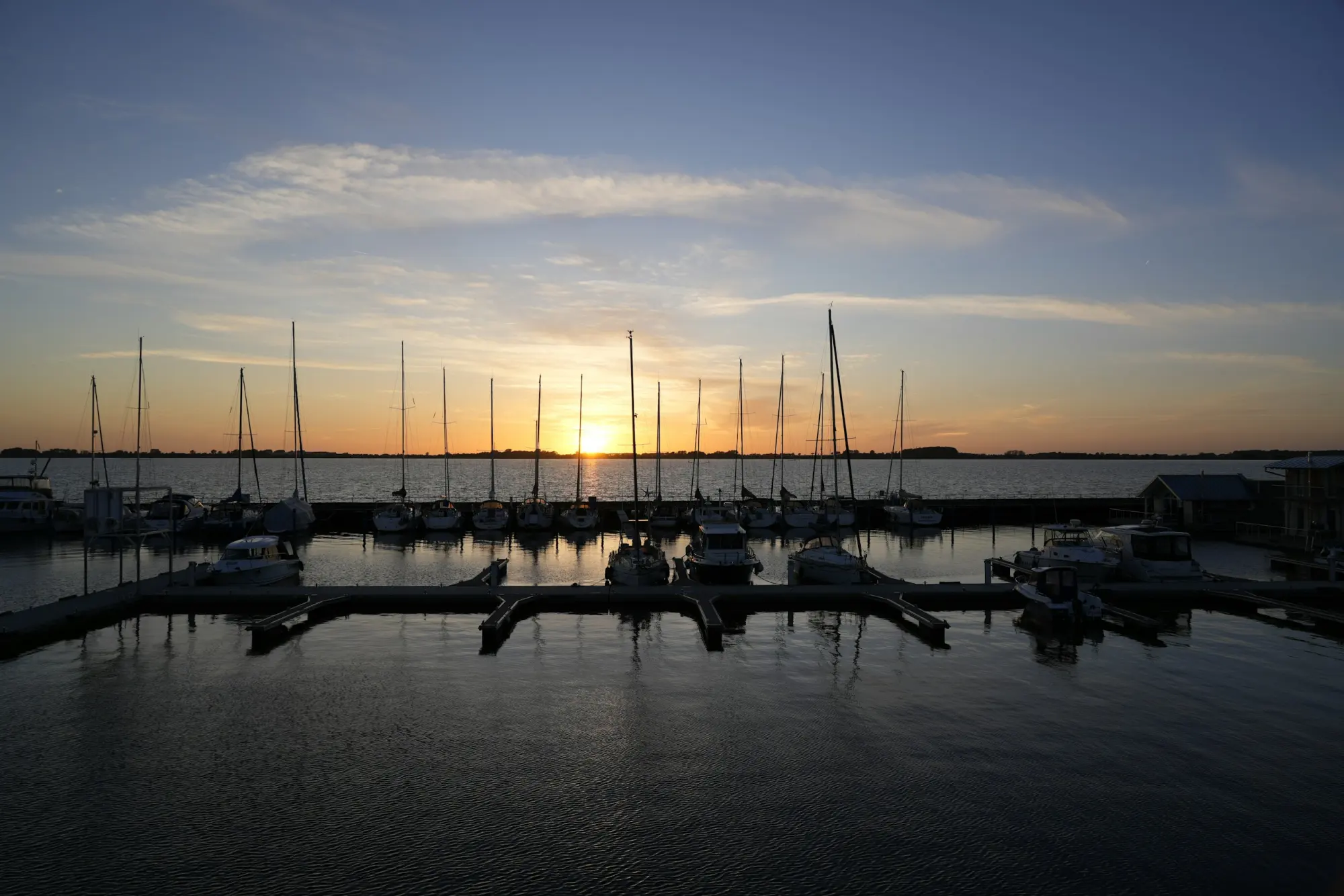 A marina at sunset, sailing yachts moored along the breakwater