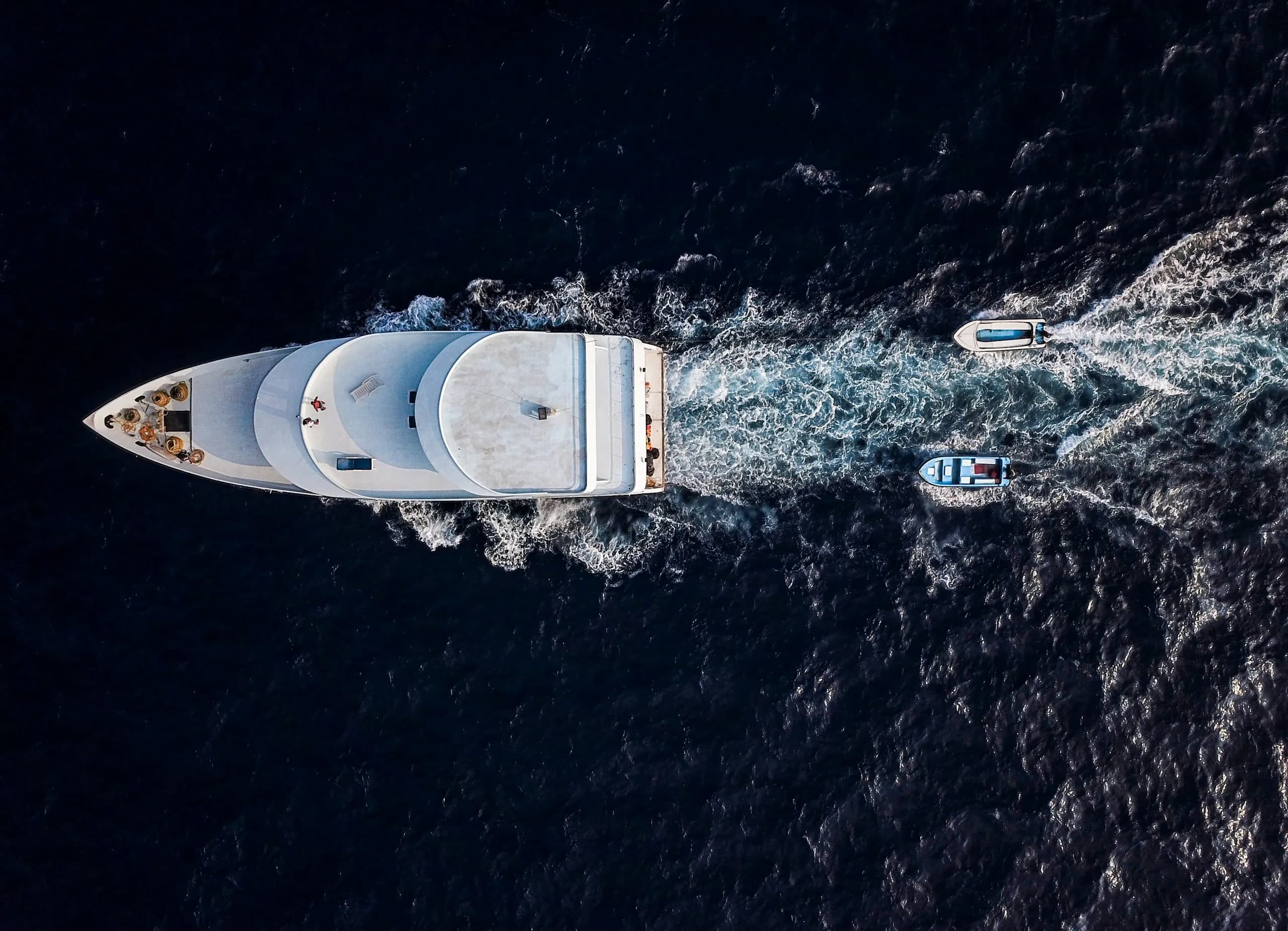 A motor yacht under way seen from directly above, two tenders following in her wake on dark blue water
